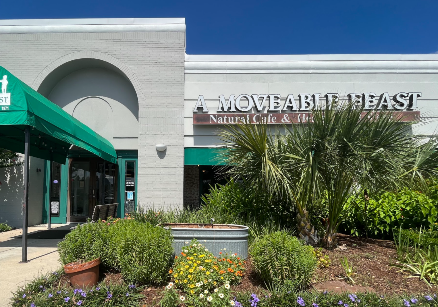 The front of out store, showing the garden, entryway, covered awning, a bench, and the double doors of the entrance