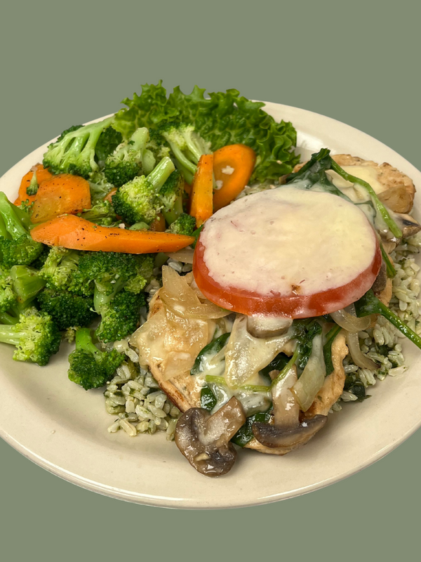 Grilled chicken topped with grilled onions, mushrooms, and jack cheese on a bed of pesto brown rice with a side of broccoli and carrots on a plate